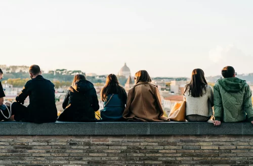 Vivir en Italia como ciudadano italiano: Foto de personas sentadas en el muro del Jardín de los Naranjos, disfrutando de la vista de Roma.