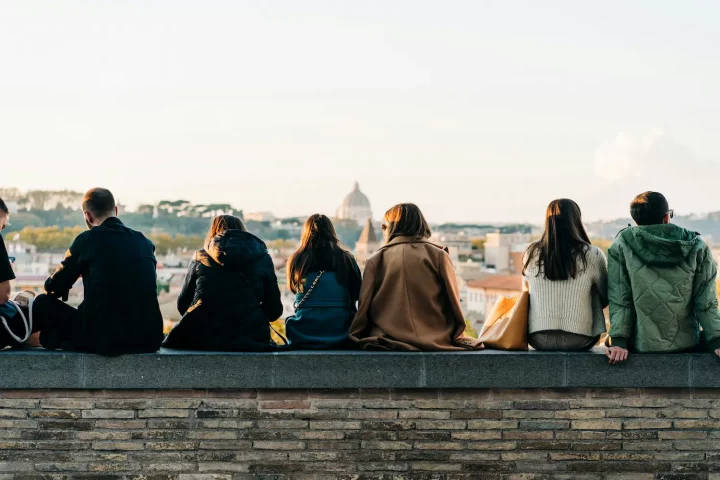 Vivir en Italia como ciudadano italiano: Foto de personas sentadas en el muro del Jardín de los Naranjos, disfrutando de la vista de Roma.